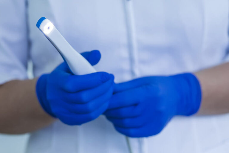Intraoral camera device being held by a dentist wearing blue gloves