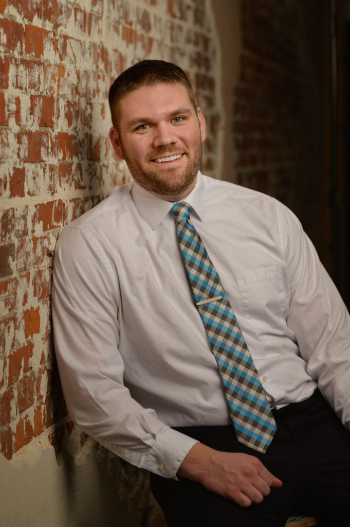 Dr. Cory Wilkinson, dentist at Healthy Smiles Family Dentistry smiling and leaning on brick wall