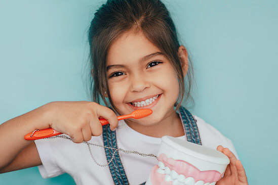 child smiling holding a toothbrush near their baby teeth