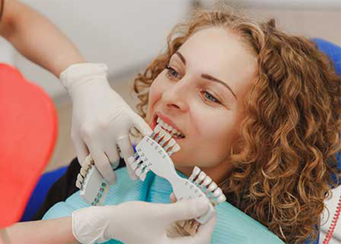 female sites in a dental chair while the dentist compares which shade of tooth color matches the patient's teeth