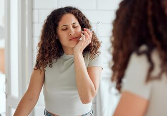 Toothache, oral discomfort and dental sensitivity for a woman in pain while brushing her teeth in the morning. African American female suffering with a painful, hurting or inflammation in her mouth